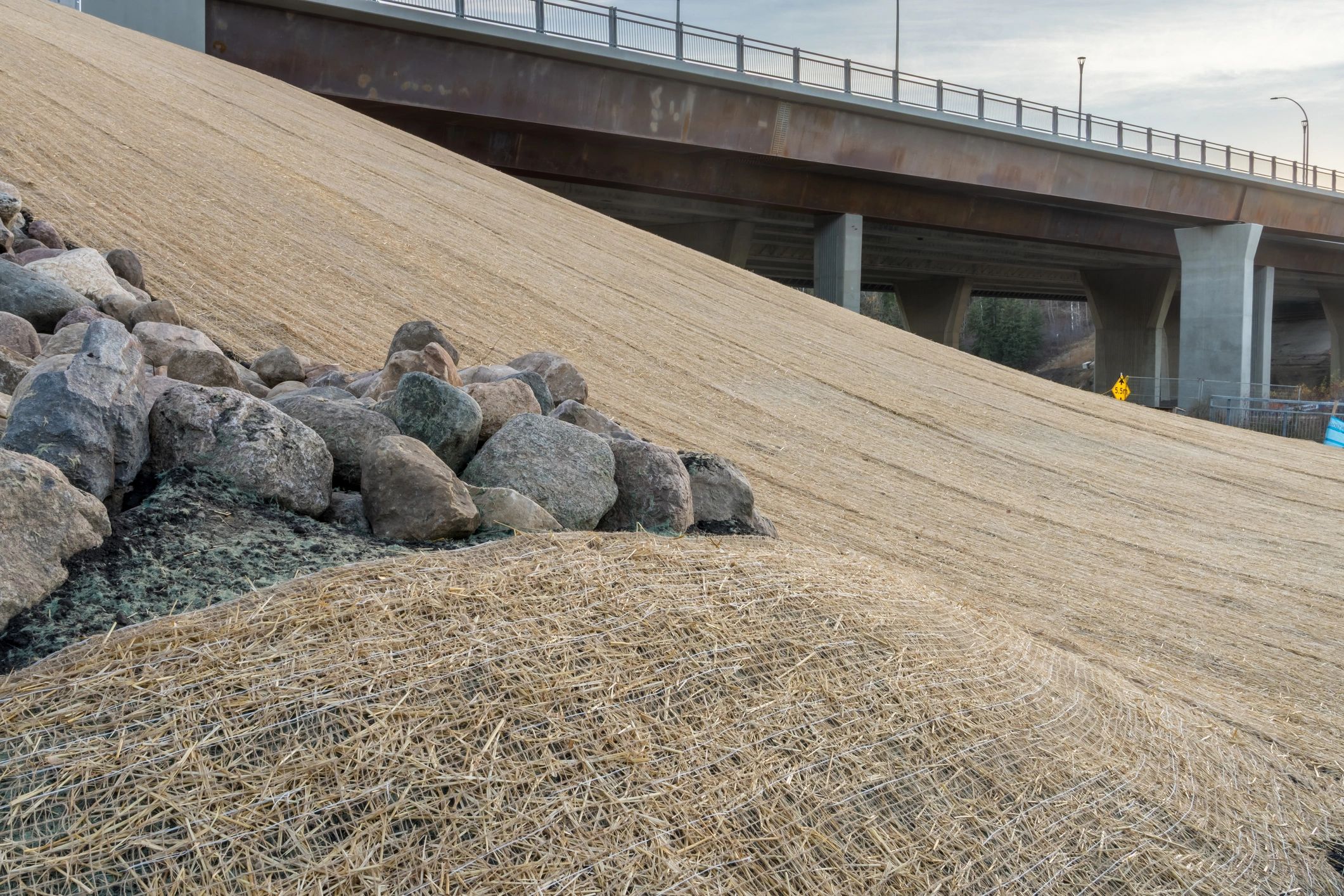 Bridge over straw-covered slope and rocks.