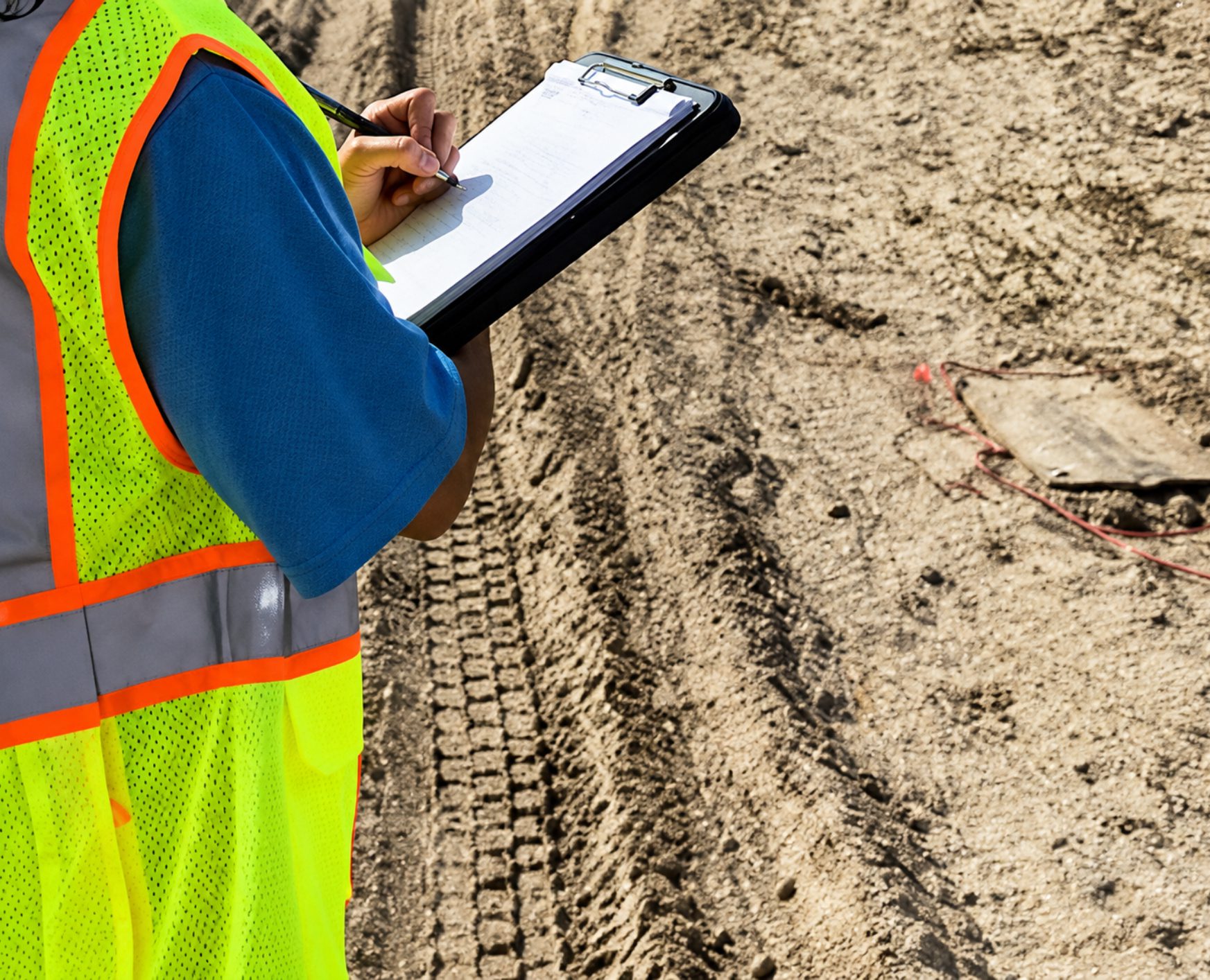 Worker writing on clipboard at construction site.