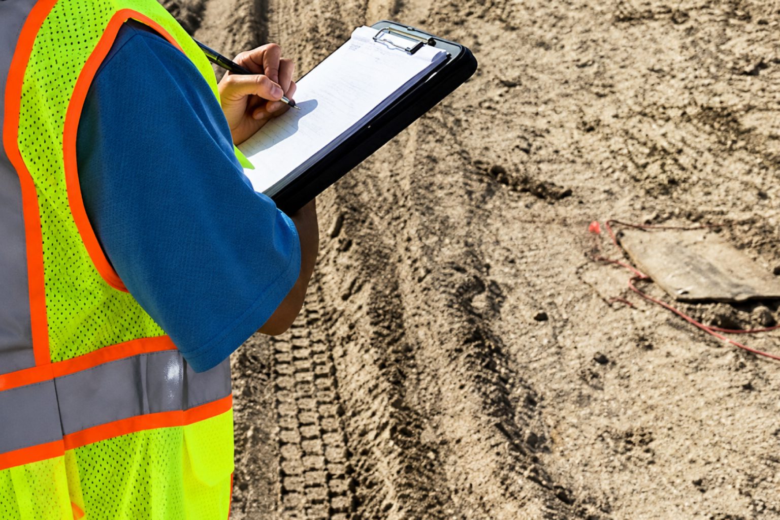 Worker writing on clipboard at construction site.